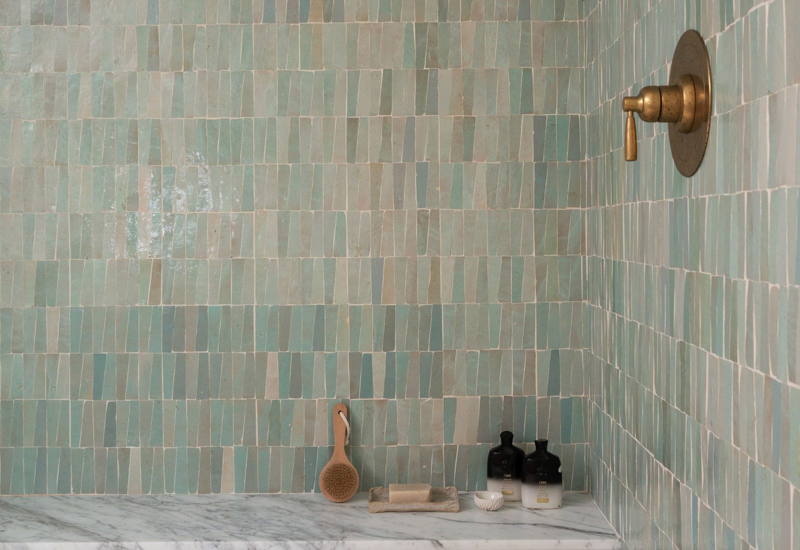 Shower wall clad in sea green handmade zellige tiles with brass fixtures